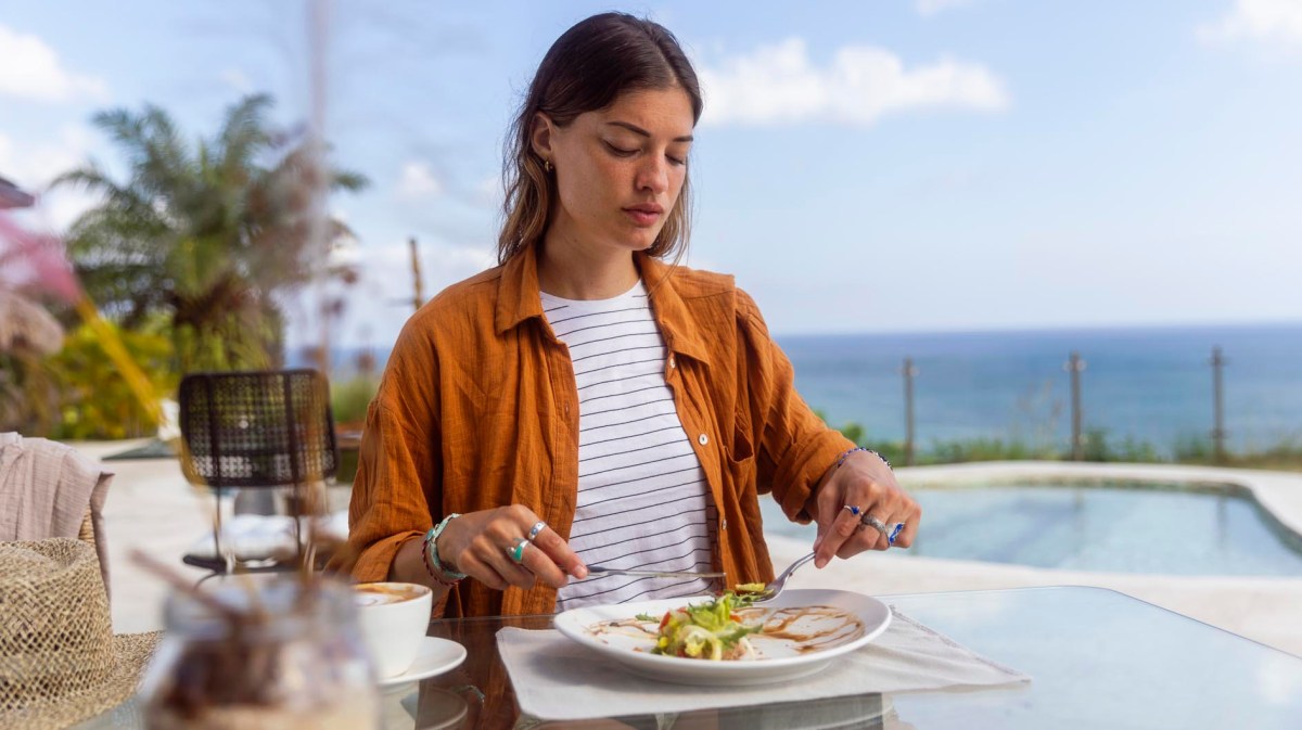 Frau sitzt im Urlaub im Hotelrestaurant und isst etwas vom Buffet.