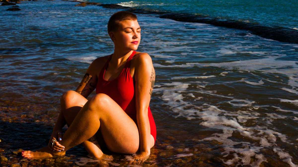 Junge Frau sitzt im Badeanzug an Strand.