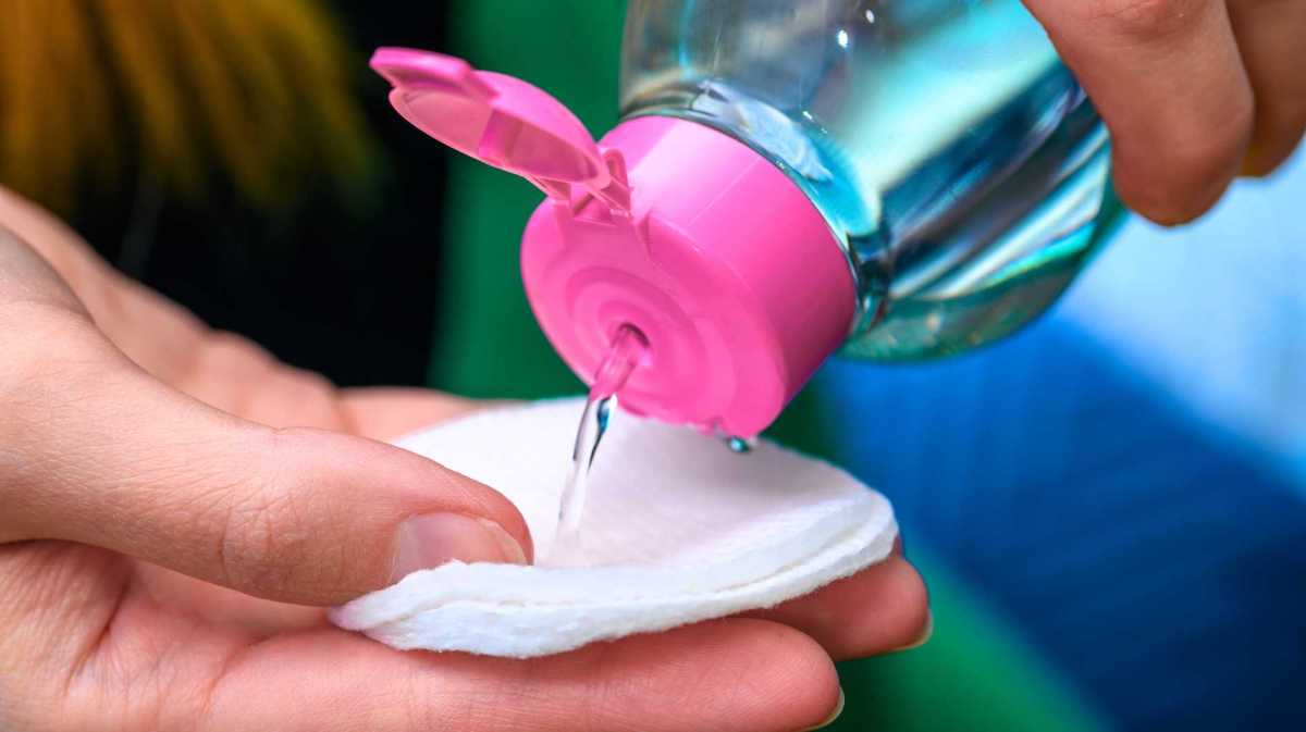 Person schüttet Nagellackentferner auf Wattepad - Nahaufnahme.