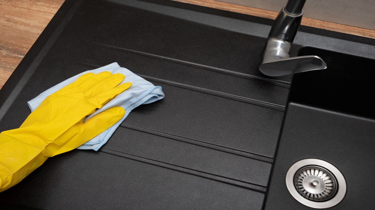 Gelber Handschuh putzt mit Lappen schwarzes Spülbecken