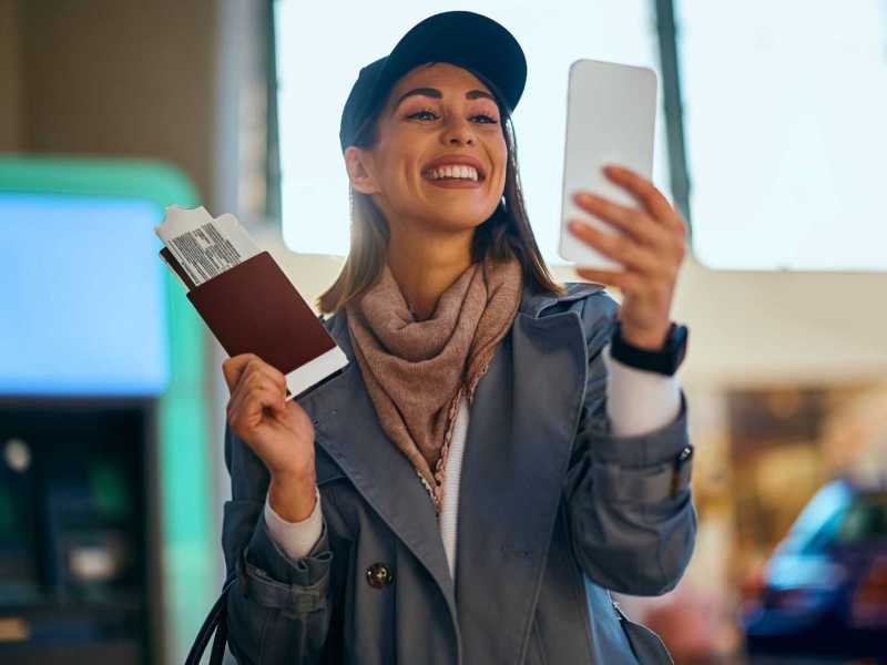 Junge Frau macht ein Selfie am Flughafen mit ihrem Boardingticket.