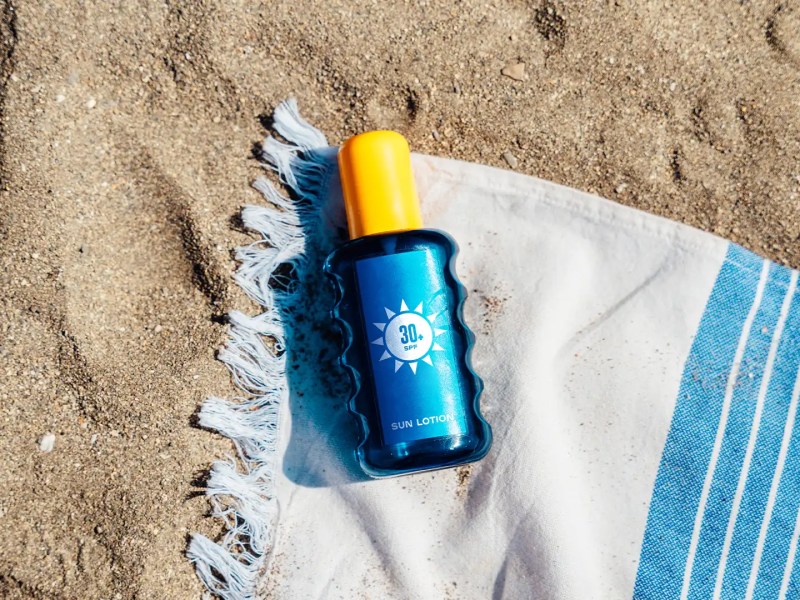 Blaue Sonnencreme-Tube liegt auf Handtuch am Strand