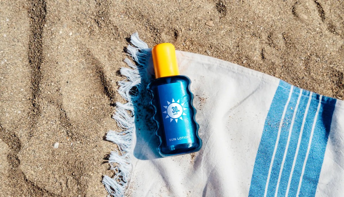 Blaue Sonnencreme-Tube liegt auf Handtuch am Strand