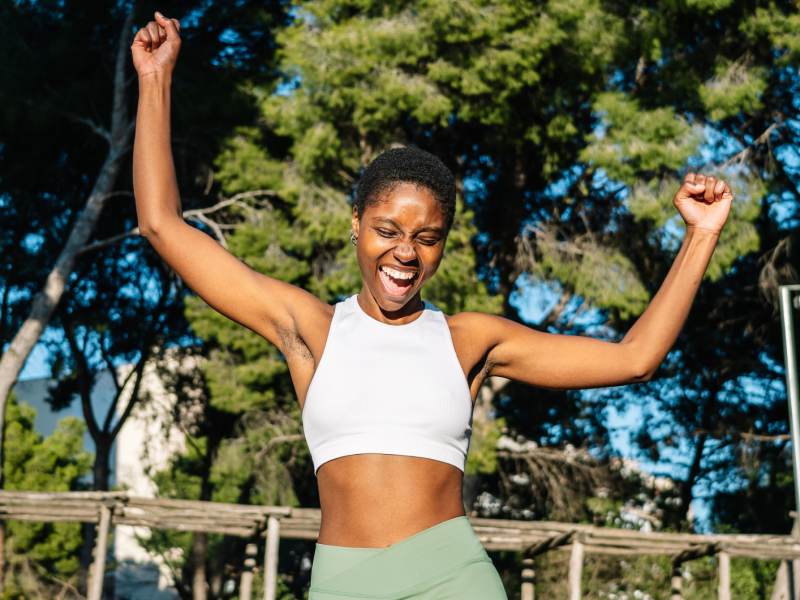 Glückliche Sportlerin, die ihren Sieg in einem Park feiert und die Arme hebt