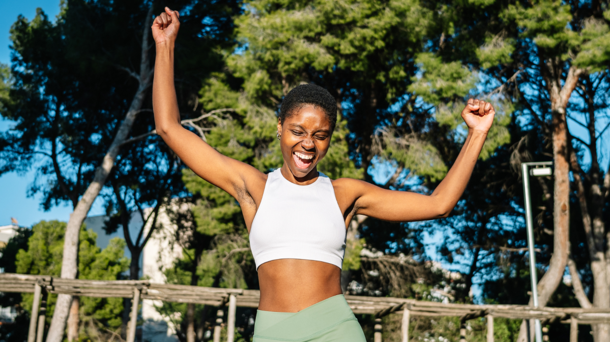 Glückliche Sportlerin, die ihren Sieg in einem Park feiert und die Arme hebt