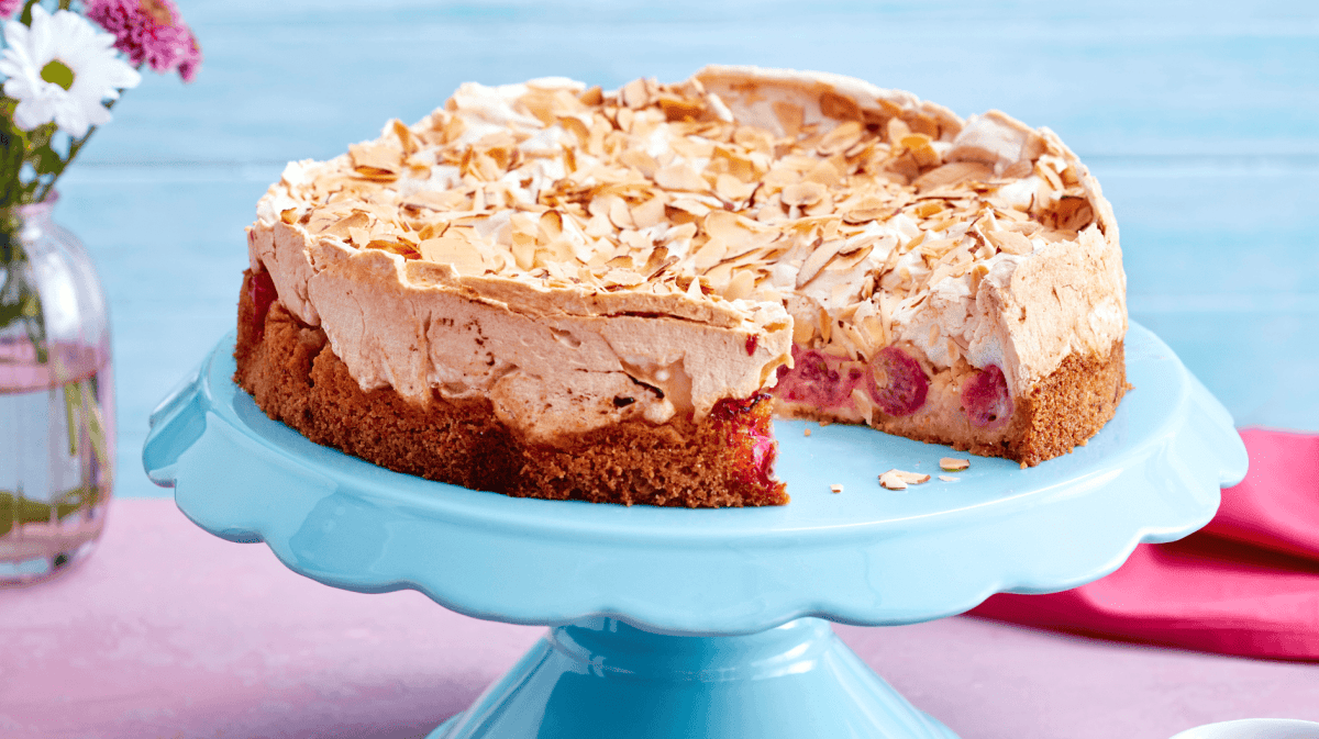 Stachelbeerkuchen mit Baiserhaube auf blauem Kuchenständer.