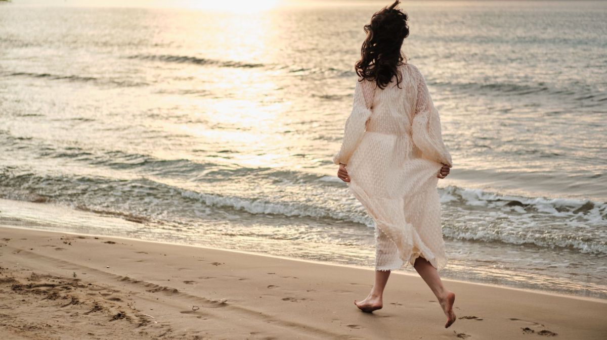 Frau in weißem Kleid läuft am Strand entlang