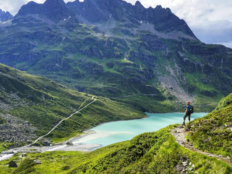Wanderer steht vor einer Bergkulisse und einem Bergsee.