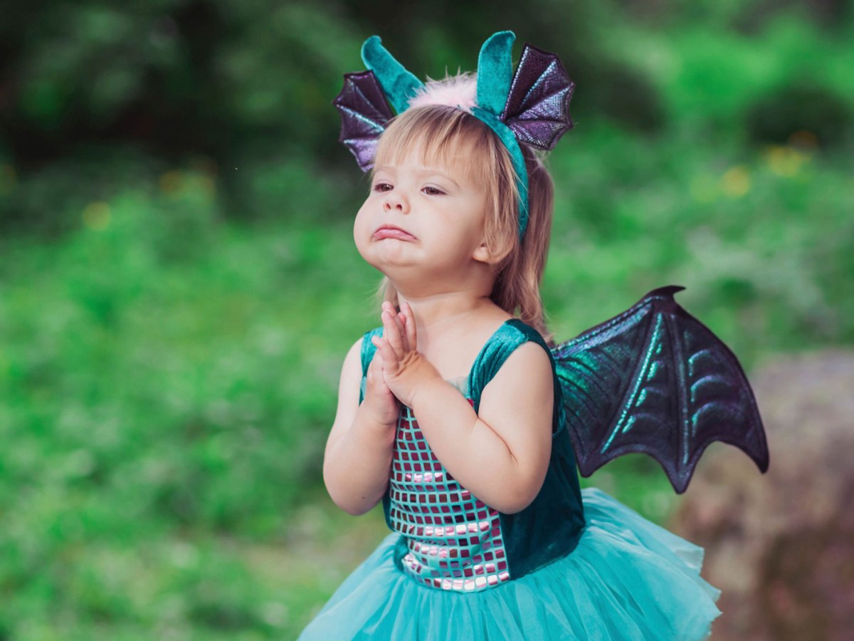 Kleines M&auml;dchen im Drachenkost&uuml;m steht im Wald und bettelt um etwas, das es haben m&ouml;chte.