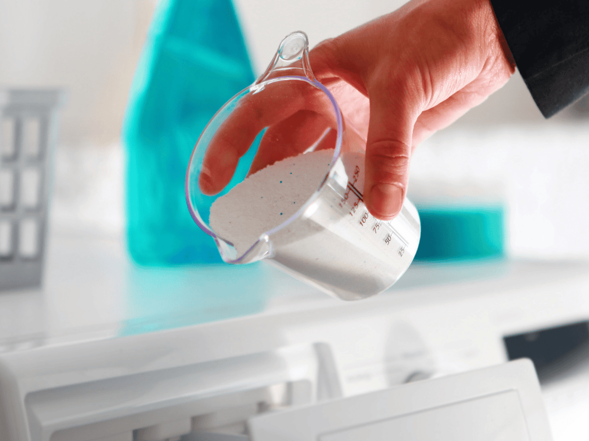 Person sch&uuml;ttet Waschmittel in Waschmaschine.