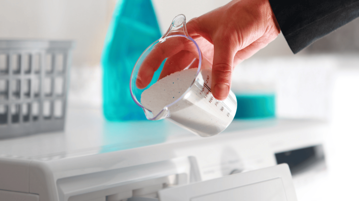 Person schüttet Waschmittel in Waschmaschine.