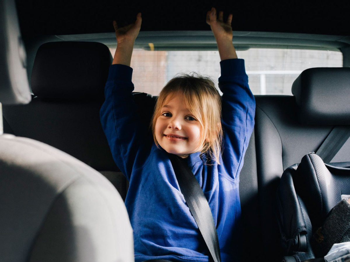 M&auml;dchen auf der R&uuml;ckbank im Auto lacht freundlich in die Kamera.
