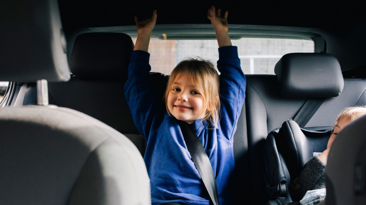 Mädchen auf der Rückbank im Auto lacht freundlich in die Kamera.