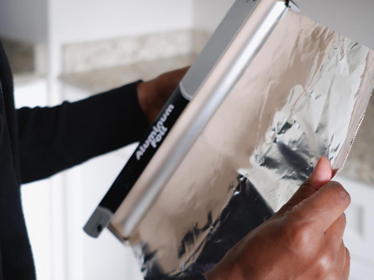 Frau rei&szlig;t Alufolie von einer Rolle.