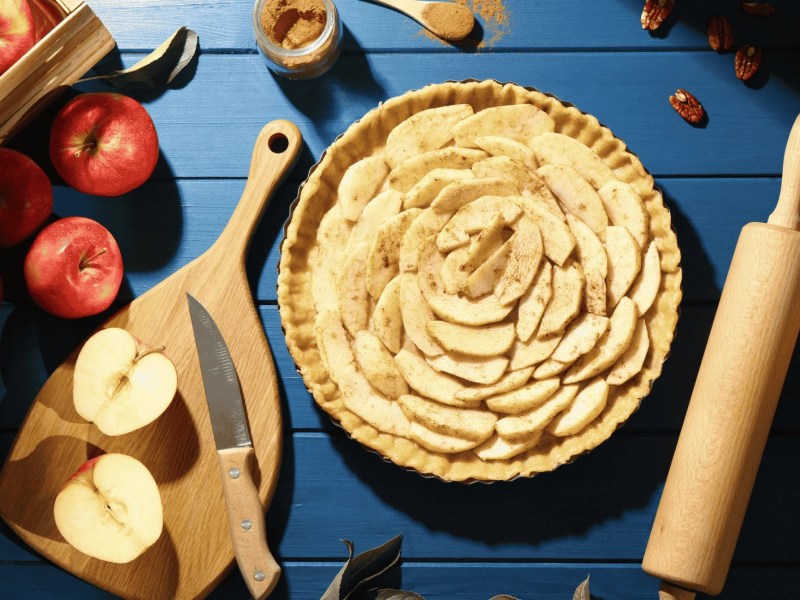 Ungebackener hausgemachter Apfelkuchen und Zutaten auf blauem Holztisch, flach liegen