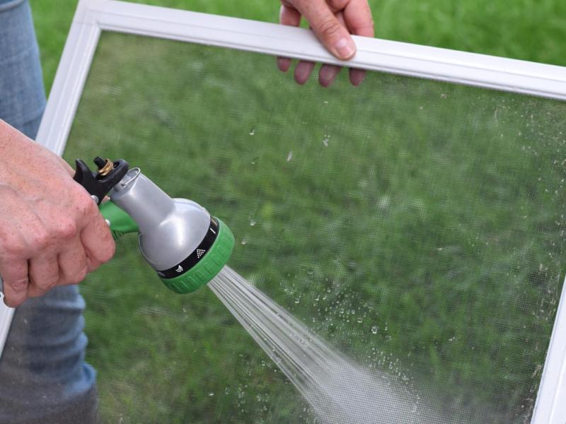 Person duscht Fliegengitter mit einem Wasserschlauch im Garten ab.