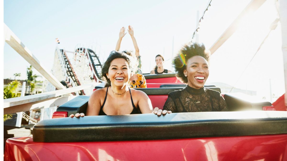 Zwei Frauen sitzen in einer Achterbahn und freuen sich.