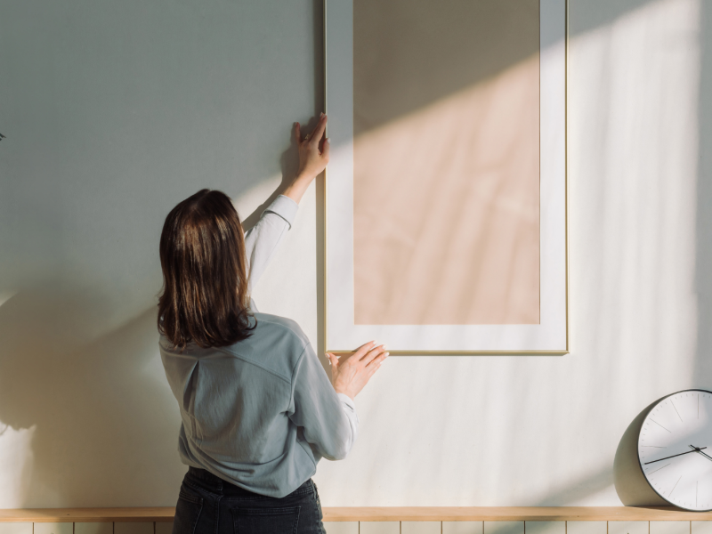 Frau dekoriert ihre Wand mit hellem Bilderrahmen.