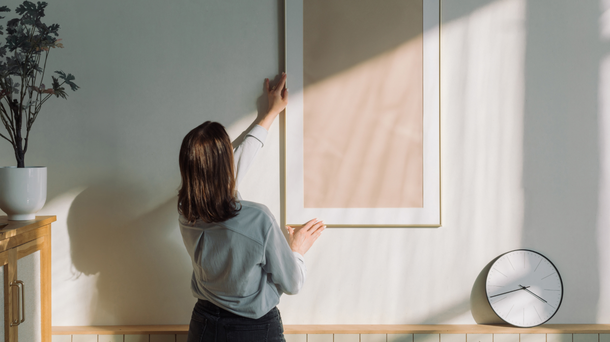 Frau dekoriert ihre Wand mit hellem Bilderrahmen.