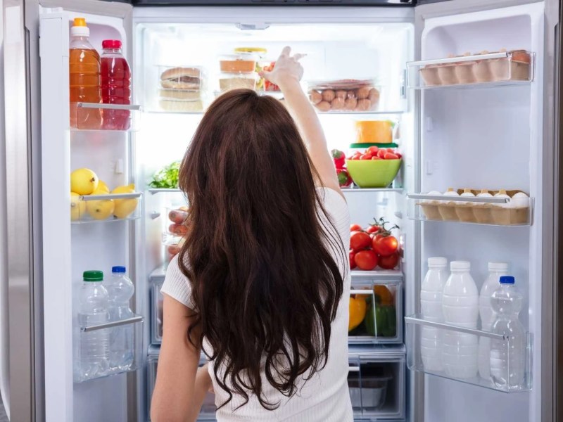 Frau steht vor sortiertem Kühlschrank