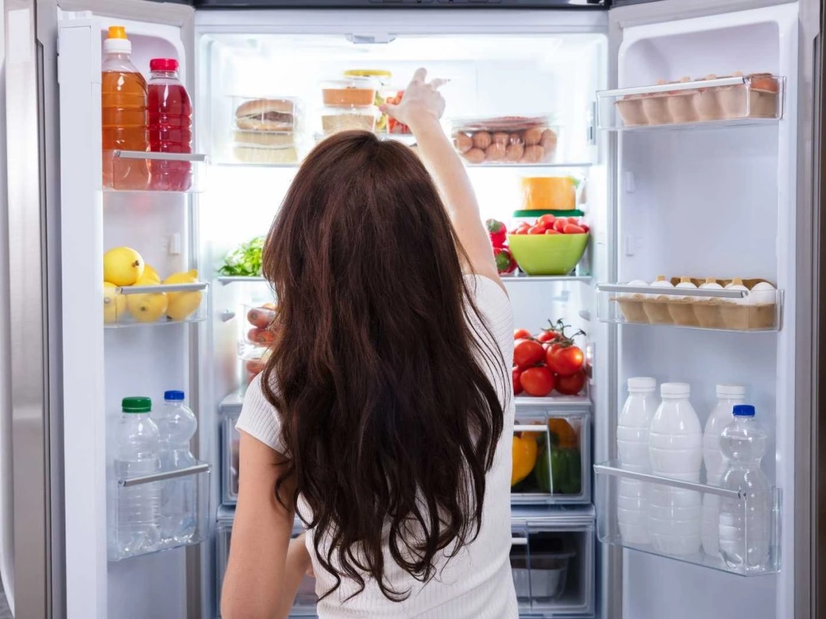 Frau steht vor sortiertem Kühlschrank