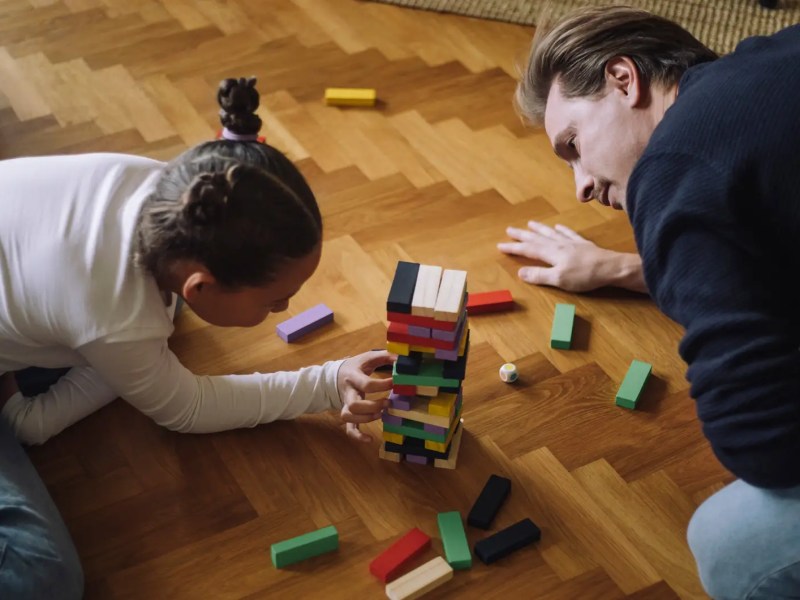 Vater und Tochter spielen Jenga auf dem Fu&szlig;boden.