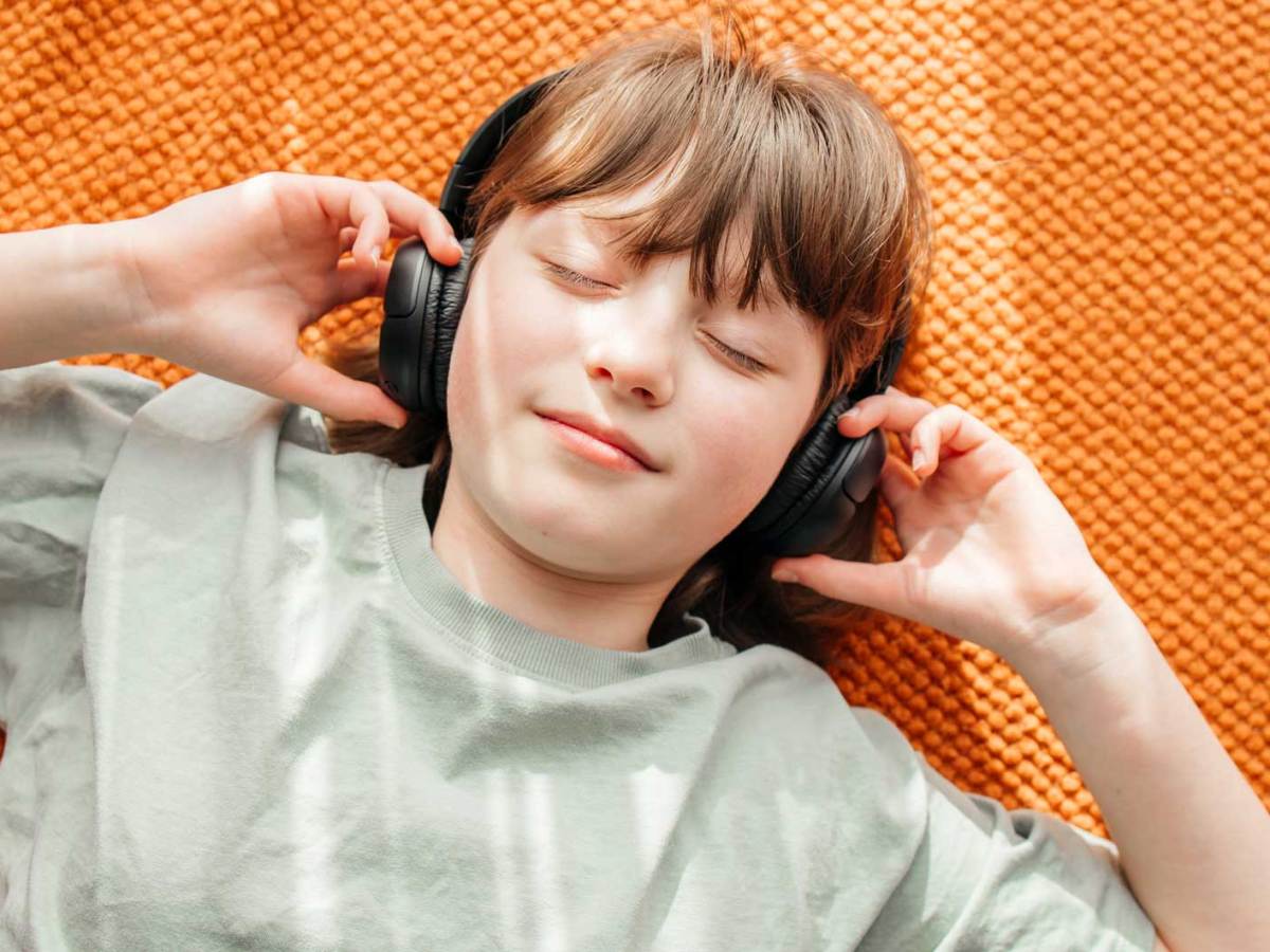 Mädchen liegt auf dem Fußboden, hat die Augen geschlossen und trägt On-ear-Kopfhörer.