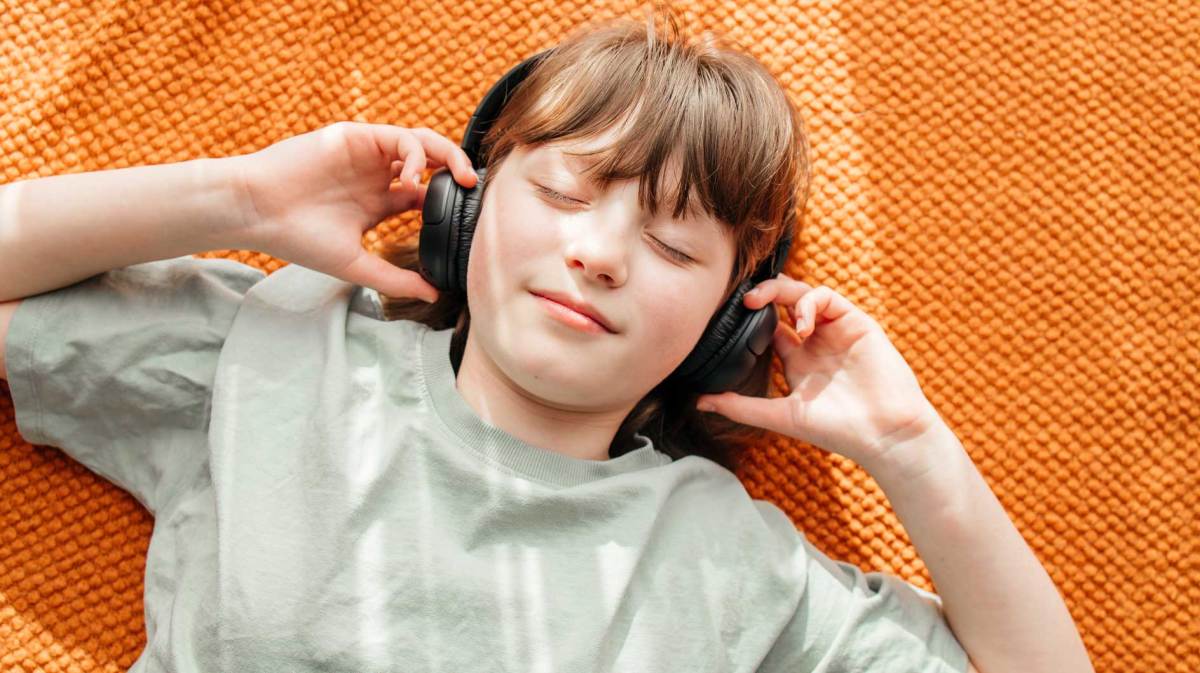 Mädchen liegt auf dem Fußboden, hat die Augen geschlossen und trägt On-ear-Kopfhörer.