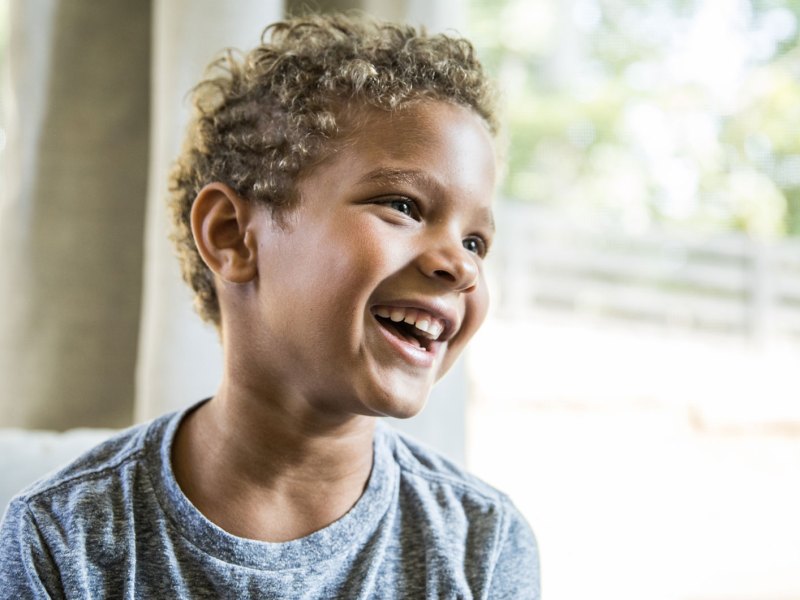 Porträt eines Jungen im grauen Shirt, der fröhlich und sorglos lacht.
