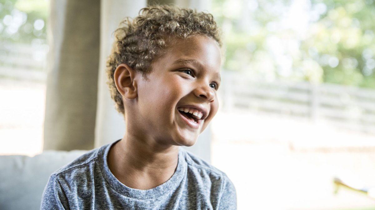Porträt eines Jungen im grauen Shirt, der fröhlich und sorglos lacht.