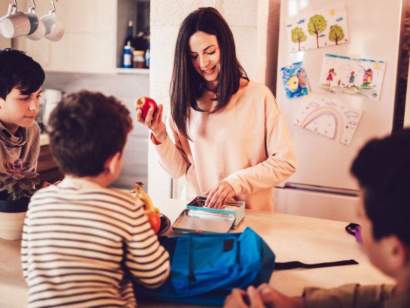 Mutter packt die Brotdosen der Kinder am Abend, die Kids und der Vater gucken zu.