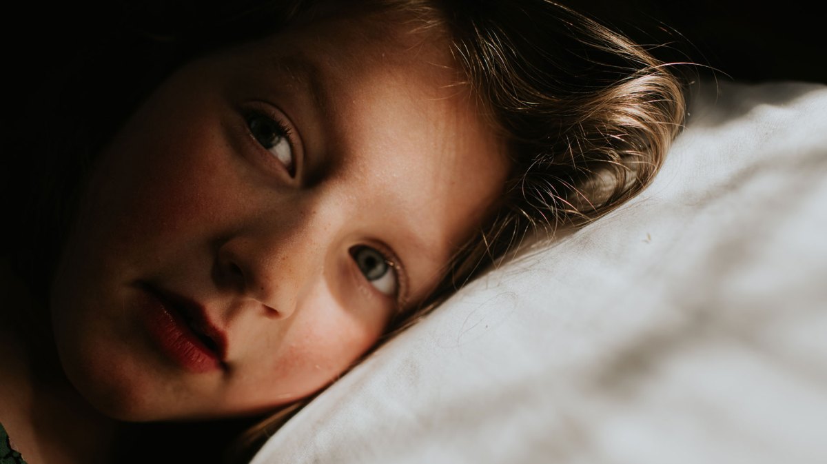 Nahaufnahme eines Mädchens. Sein Kopf liegt auf einem weißen Kissen.