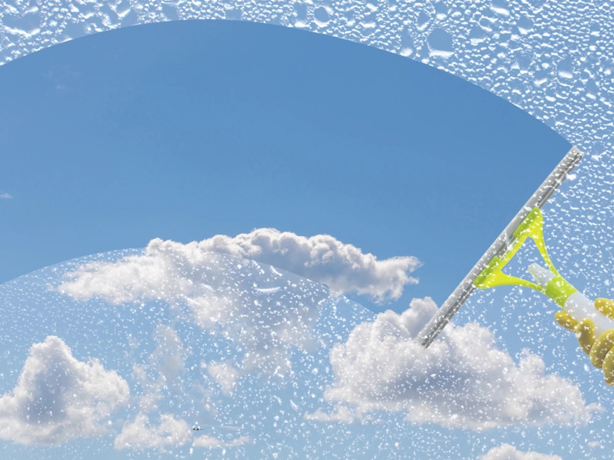 Hand in gelbem Gummihandschuh wischt mit Fensterabzieher Schaum von Scheibe und gibt den Blick auf blauen Himmel frei.