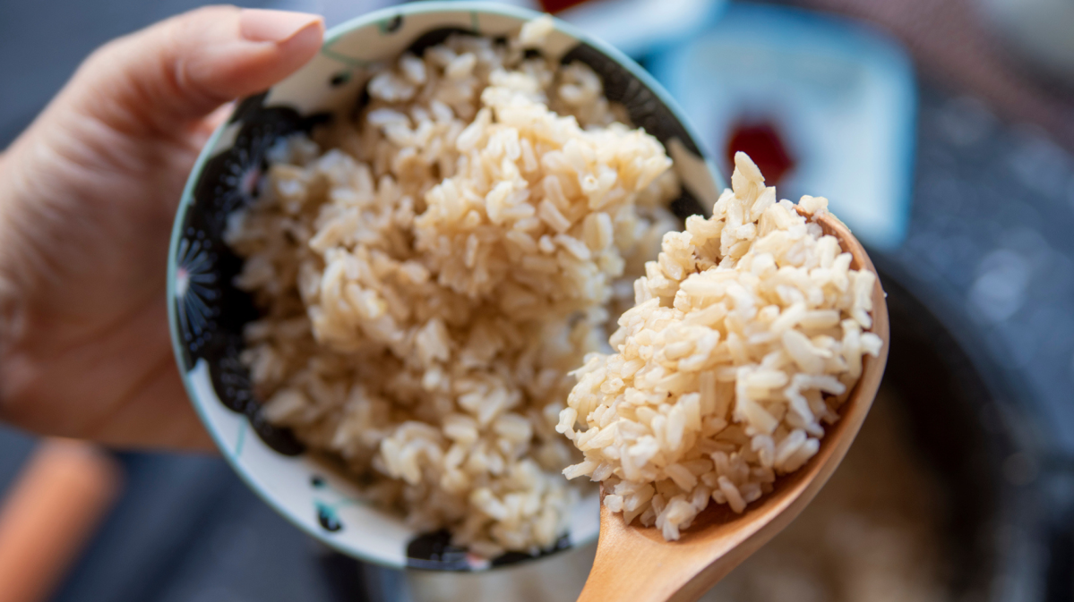 Person hält eine Schale und einen Holzkochlöffel mit Reis in den Händen.