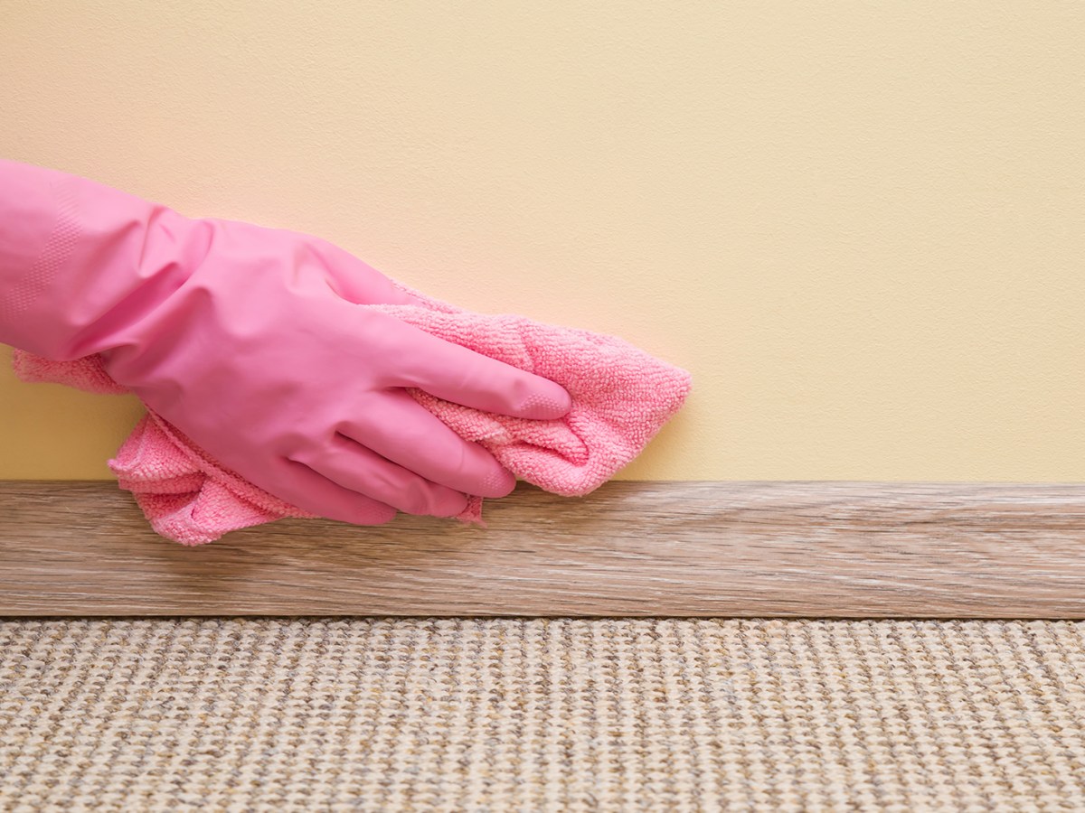 Frau tr&auml;gt pinkfarbene Handschuhe zum Putzen der Fu&szlig;leisten mit einem blauen Tuch