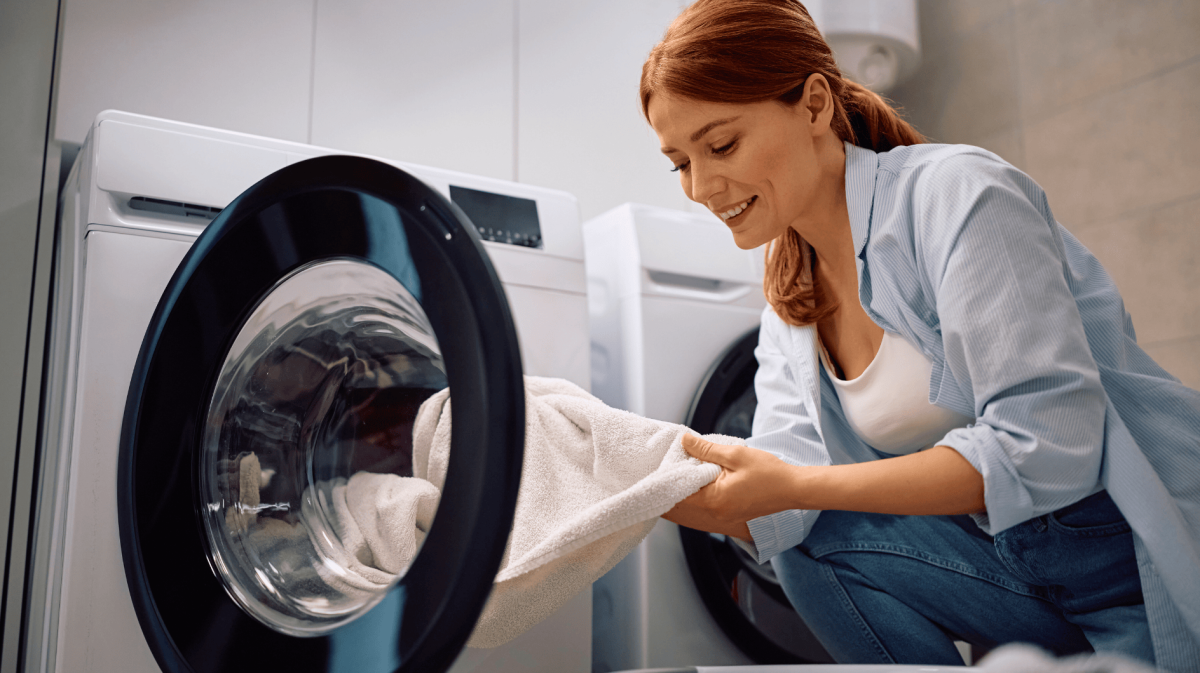 Rothaarige Frau nimmt weißes Handtuch aus ihrer Waschmaschine.
