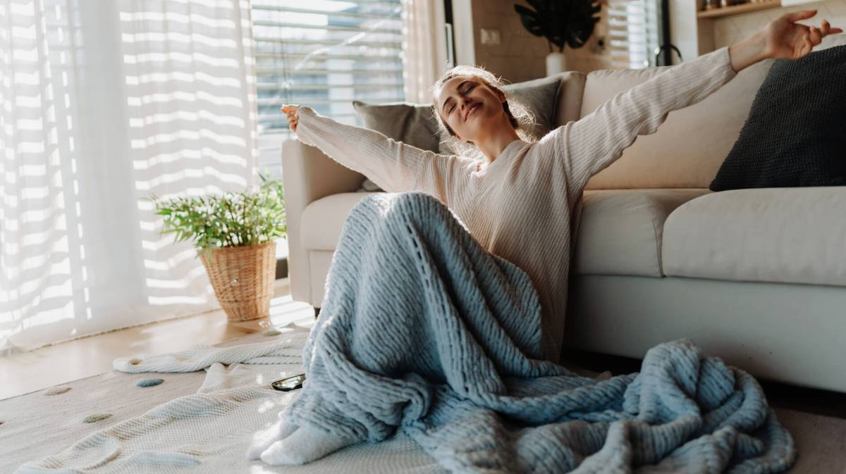 Frau sitzt in einer gemütlichen Wohnung, mit einer Decke auf ihrem Schoß