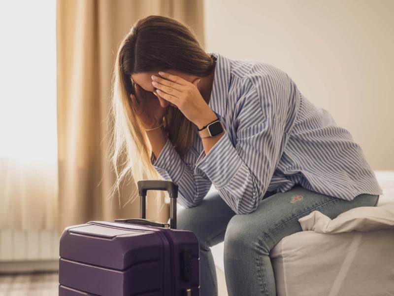 Frau sitzt im Hotelzimmer und hält sich die Hände vors Gesicht