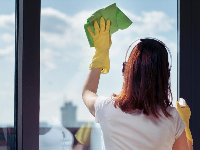 Frau putzt Fenster mit Putzhandschuhen