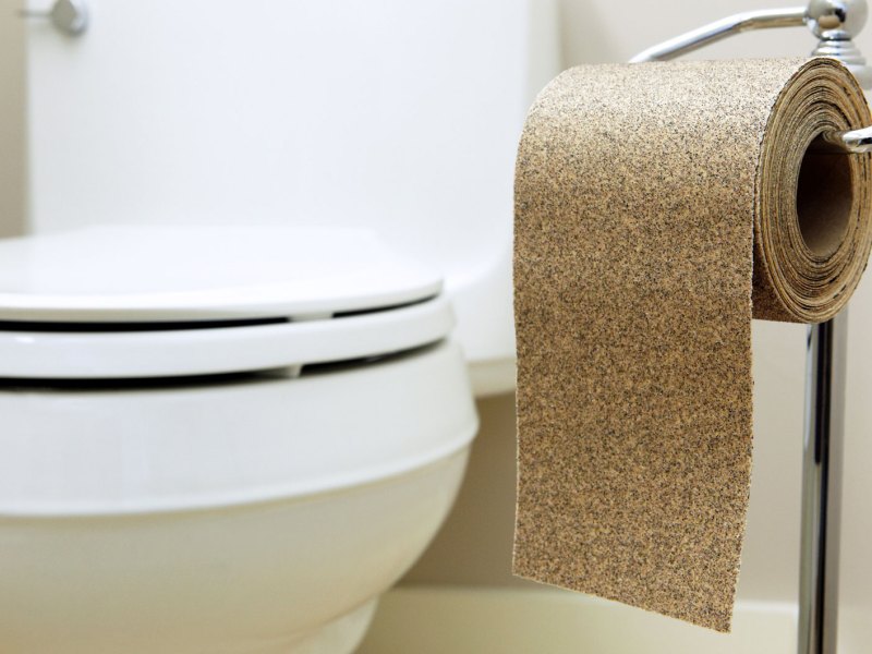 Toilette, daneben ein Klorollenständer mit einer Rolle Schleifpapier.