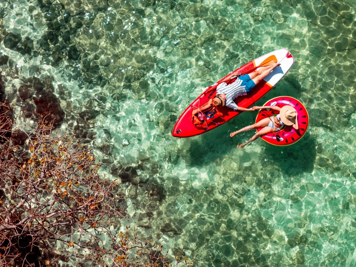 Ein junges Paar entspannt im klaren t&uuml;rkisgr&uuml;nen Wasser, sie auf einer Wassermelonen-Luftmatratze, er auf einem roten SUP