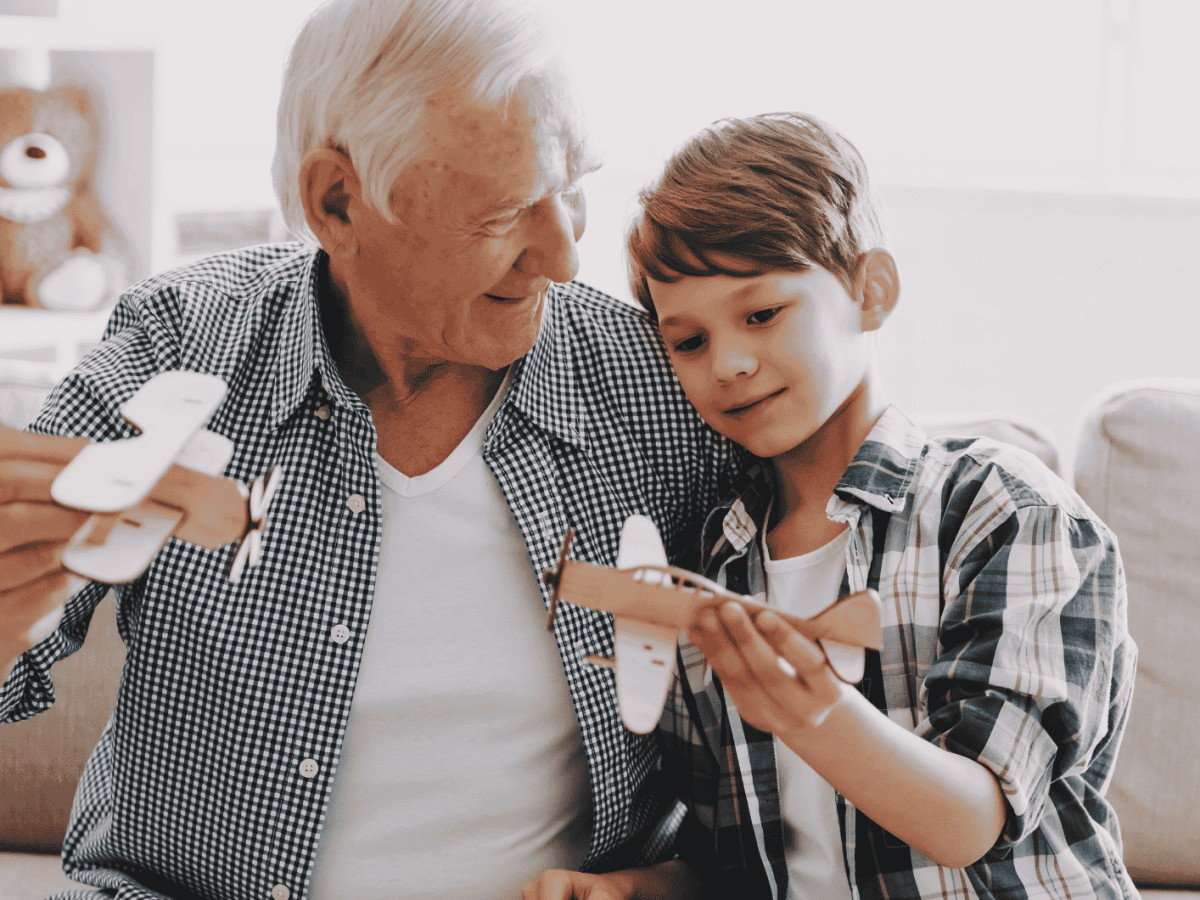 Ein Opa spielt mit seinem Enkelsohn mit gebastelten Flugzeugen.