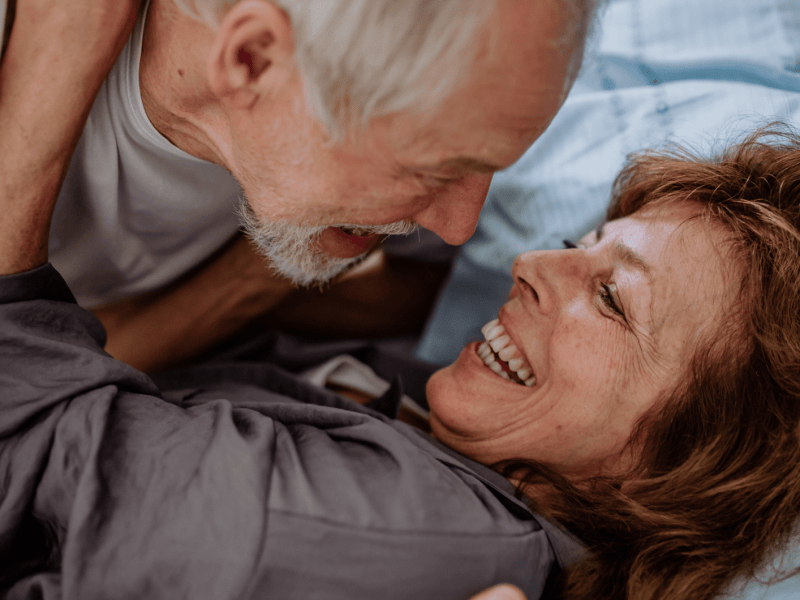 Verliebtes, älteres Paar liegt zusammen im Bett.