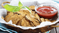 Zucchini-Parmesan-Chips auf einem Teller, daneben eine Tomatensoße.