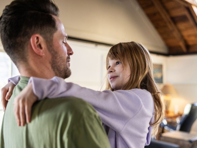 Vater hält seine Tochter auf dem Arm und beide schauen sich liebevoll in die Augen.