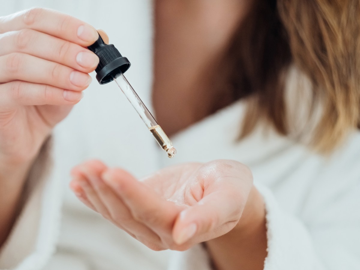 Frau die sich ein Serum mit einer Pipette in die Hand tropft.