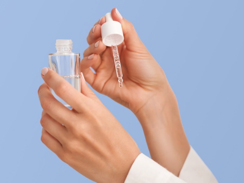 Zwei Hände mit einem Serum aus dem ein Tropfen auf die Hände fällt.