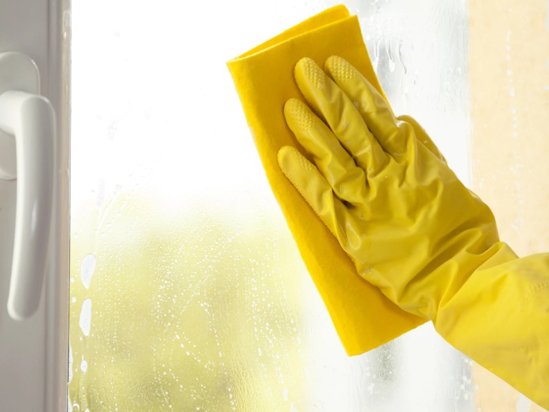 Nahaufnahme einer Hand mit gelben Handschuh, die ein Fenster putzt.