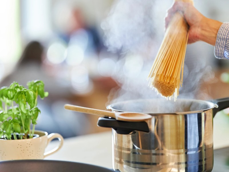 Nahaufnahme einer Hand, die Spaghetti in einen Topf auf dem Herd gibt.