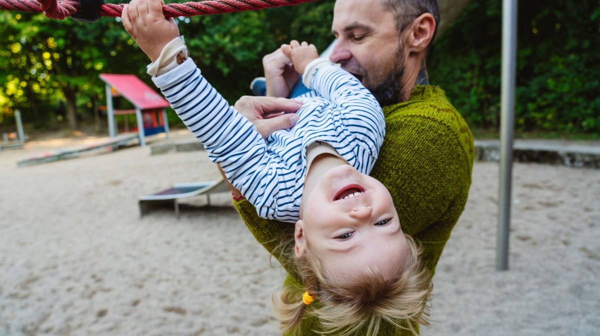 Papa und Tochter toben auf dem Spielplatz herum.